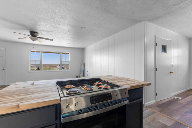 Kitchen with wood counters, a textured ceiling, ceiling fan, and stainless steel gas stove