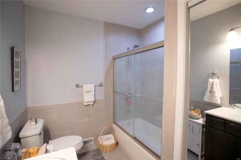 Full bathroom with toilet, tile walls, visible vents, vanity, and enclosed tub / shower combo