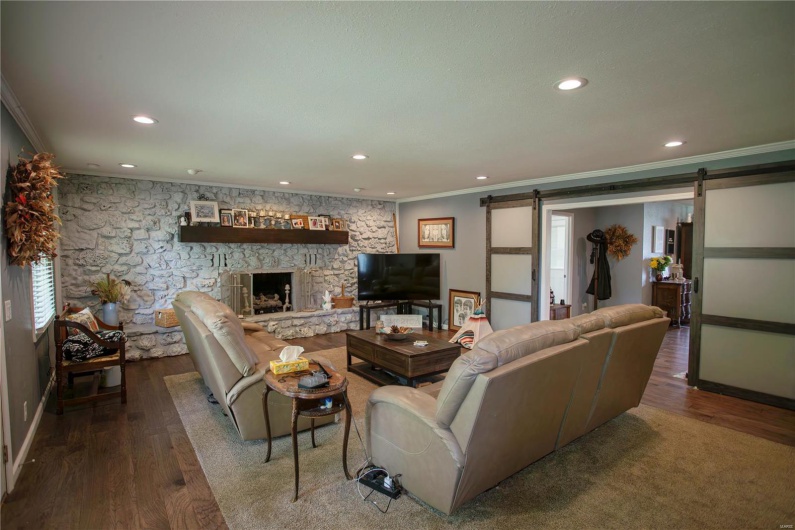 Living room featuring a barn door, baseboards, recessed lighting, wood finished floors, and ornamental molding