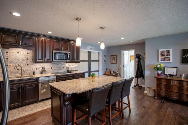 Kitchen with a sink, stainless steel appliances, backsplash, dark wood-style flooring, and light stone countertops
