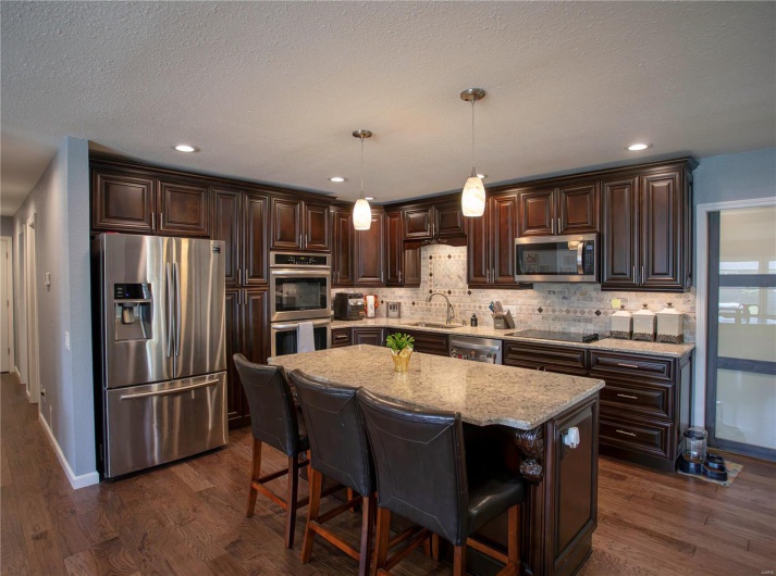 Kitchen with stainless steel appliances, dark brown cabinets, a sink, dark wood-type flooring, and decorative backsplash