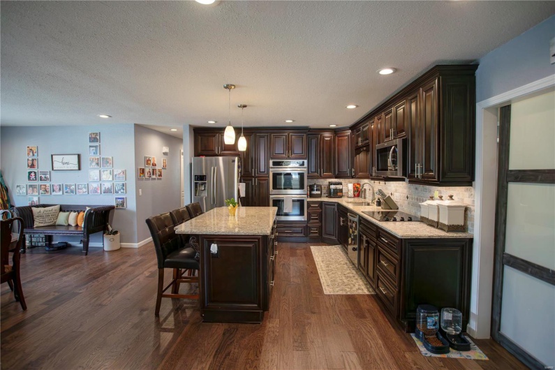 Kitchen with dark wood-style floors, light stone counters, dark brown cabinets, a kitchen island, and appliances with stainless steel finishes