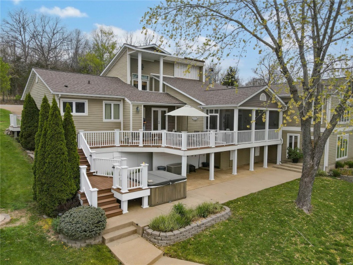 Back of property with a wooden deck, a patio area, a hot tub, stairs, and a sunroom