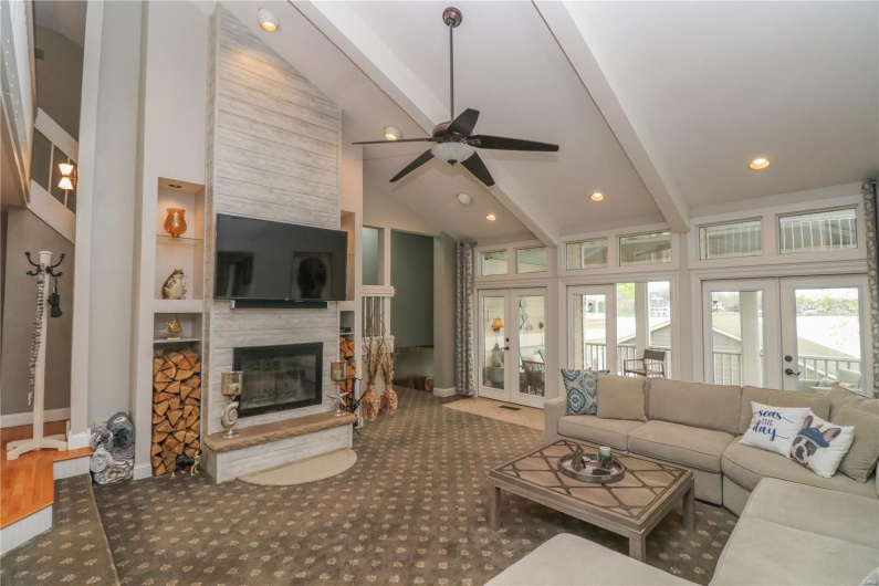 Carpeted living room featuring ceiling fan, french doors, beam ceiling, and a fireplace