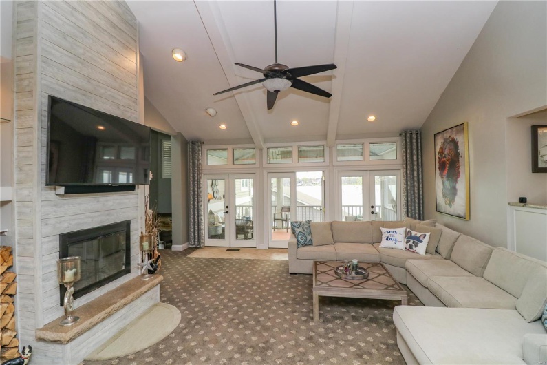 Carpeted living room with high vaulted ceiling, a large fireplace, ceiling fan, and recessed lighting