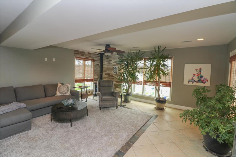 family room with a ceiling fan, a wood stove, baseboards, tile patterned flooring, and recessed lighting