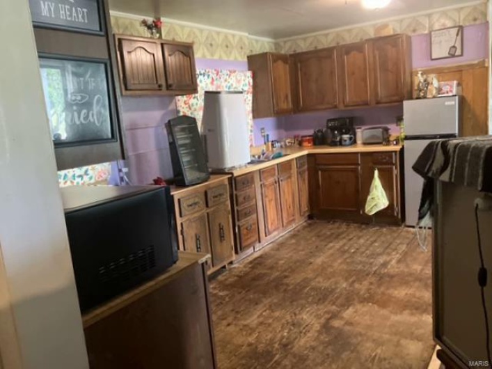 Kitchen with light countertops, freestanding refrigerator, black microwave, and wallpapered walls