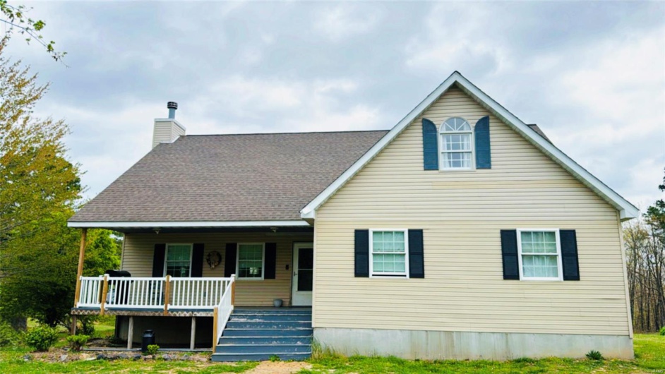 View of front of property with a front lawn, roof with shingles, a porch, and a chimney