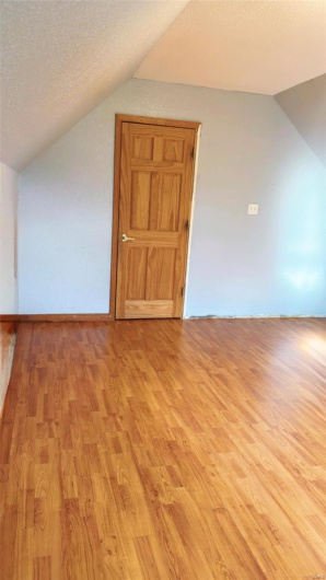 Bonus room with light wood-style floors, vaulted ceiling, and a textured ceiling