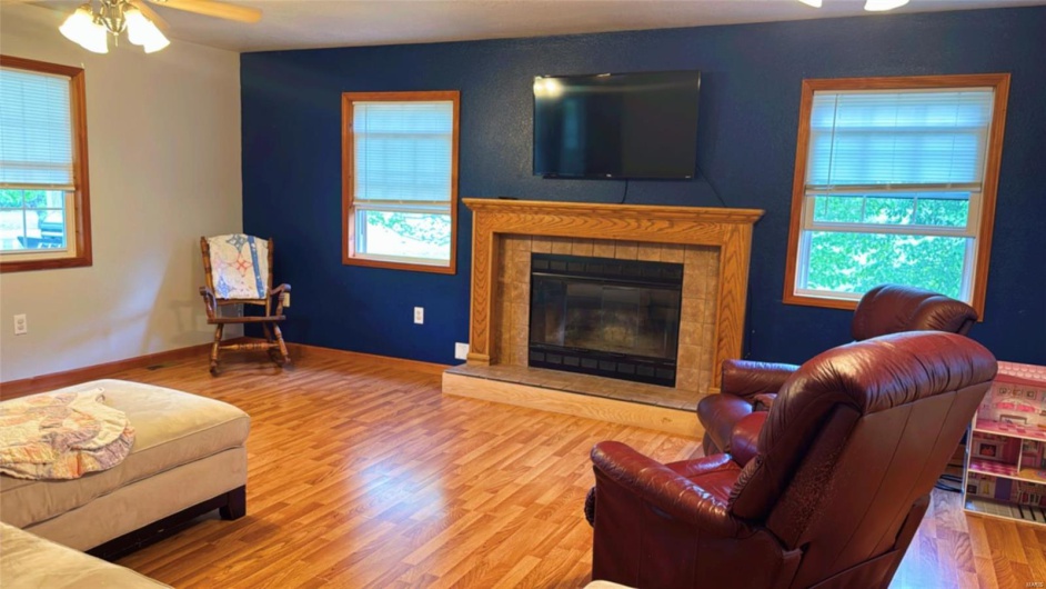 Living room featuring ceiling fan, baseboards, wood finished floors, and a fireplace