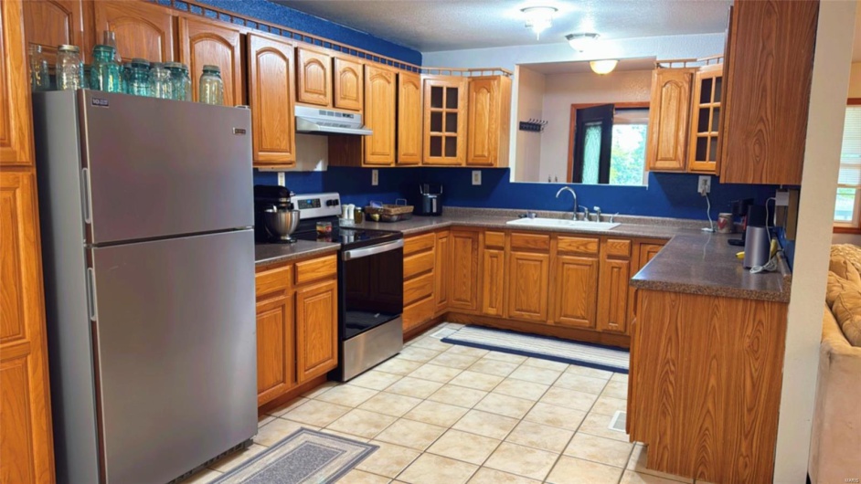Kitchen with under cabinet range hood, a sink, brown cabinets, and appliances with stainless steel finishes