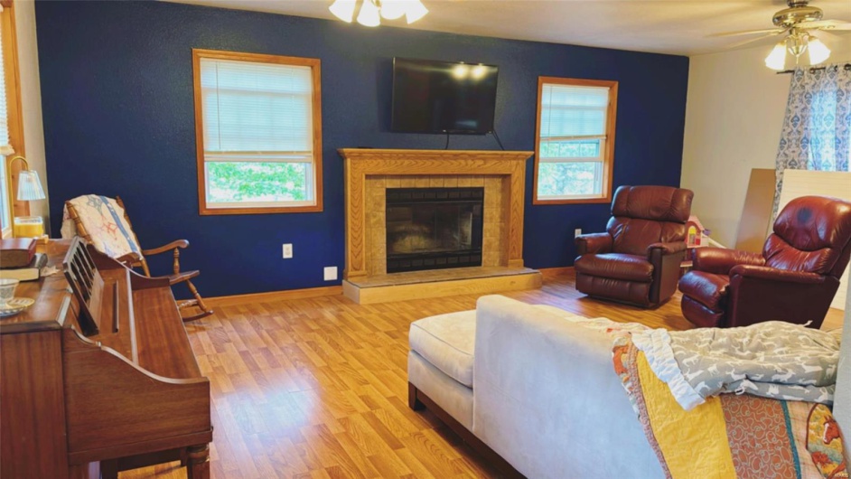 Living room featuring a glass covered fireplace, wood finished floors, a ceiling fan, and baseboards
