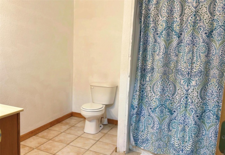 Full bathroom with baseboards, toilet, tile patterned floors, and a shower with shower curtain