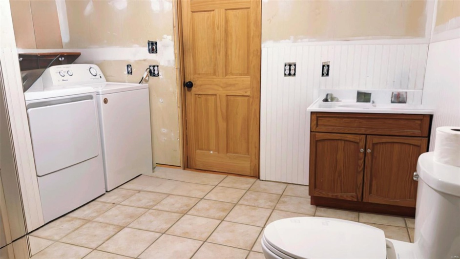 Laundry area featuring a sink, light tile patterned flooring, wainscoting, washer and dryer, and laundry area