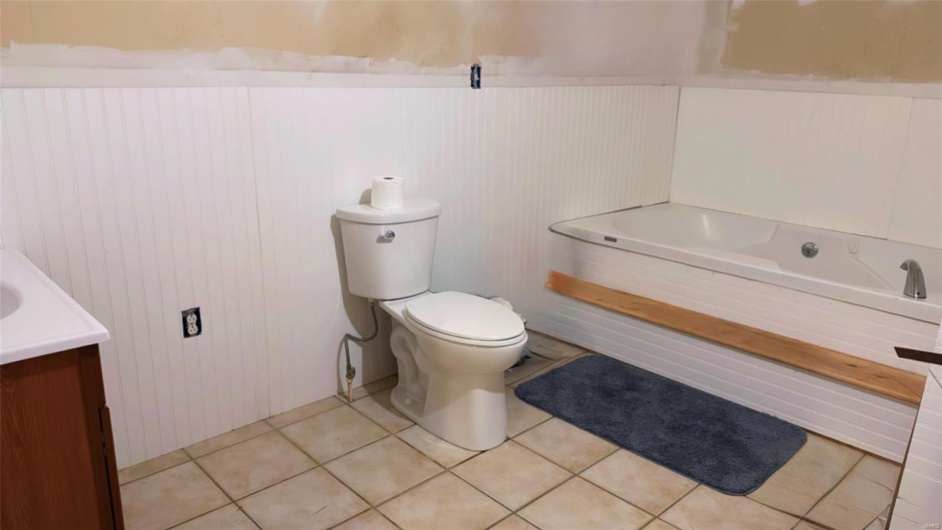 Bathroom with a wainscoted wall, toilet, a bathing tub, tile patterned flooring, and vanity