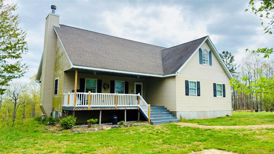 View of front of property featuring a chimney, a front lawn, a porch, and a shingled roof