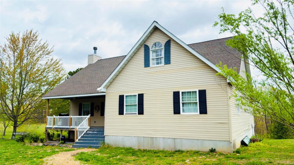 View of front of home with a chimney, a front lawn, roof with shingles, and a porch