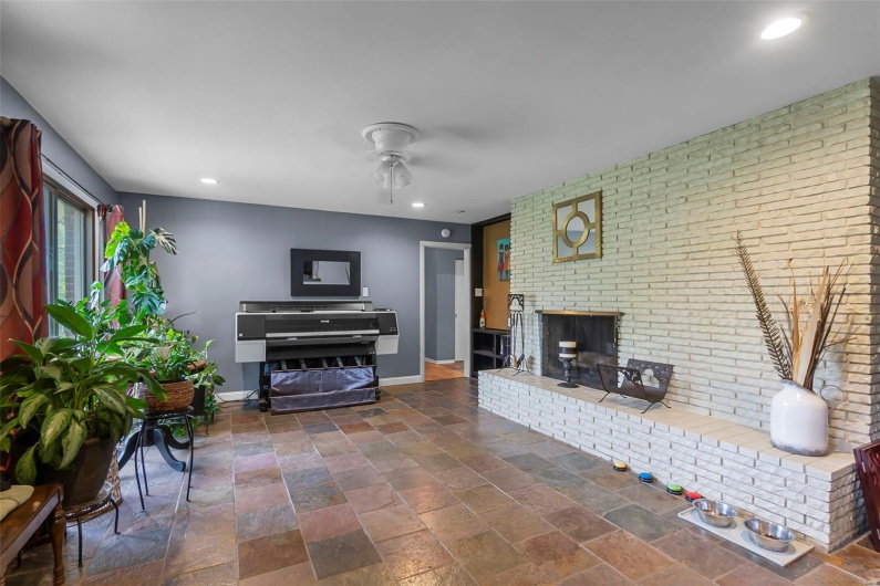 Living room with a ceiling fan, stone tile floors, baseboards, a brick fireplace, and recessed lighting