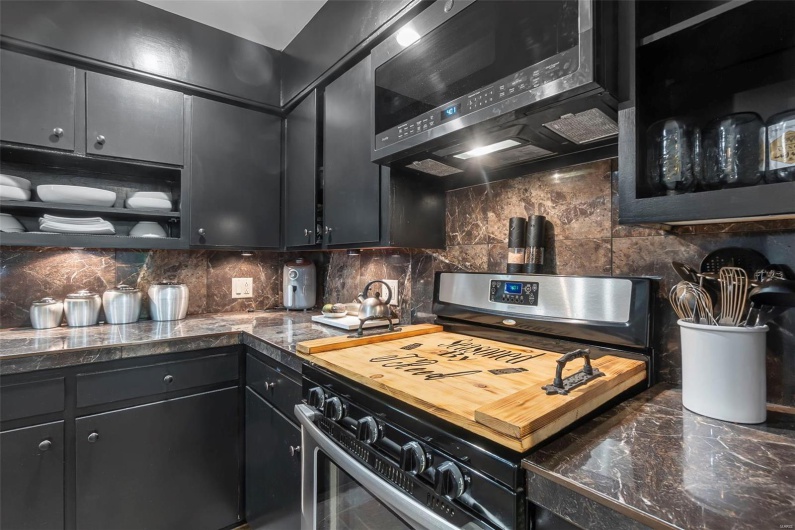 Kitchen featuring tile countertops, dark cabinets, appliances with stainless steel finishes, and tasteful backsplash