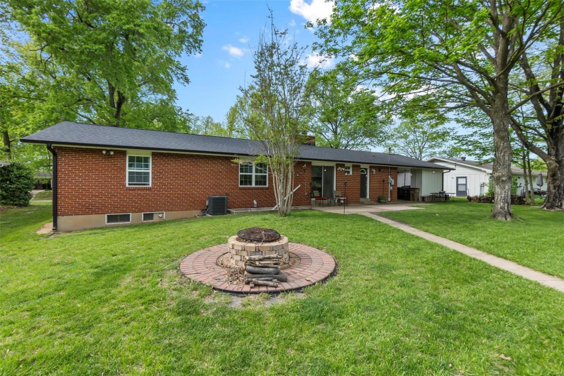Back of property featuring central air condition unit, brick siding, a yard, a patio, and an outdoor fire pit