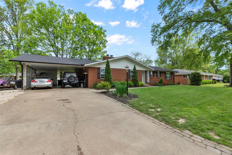 Ranch-style house featuring a chimney, driveway, a carport, brick siding, and a front yard