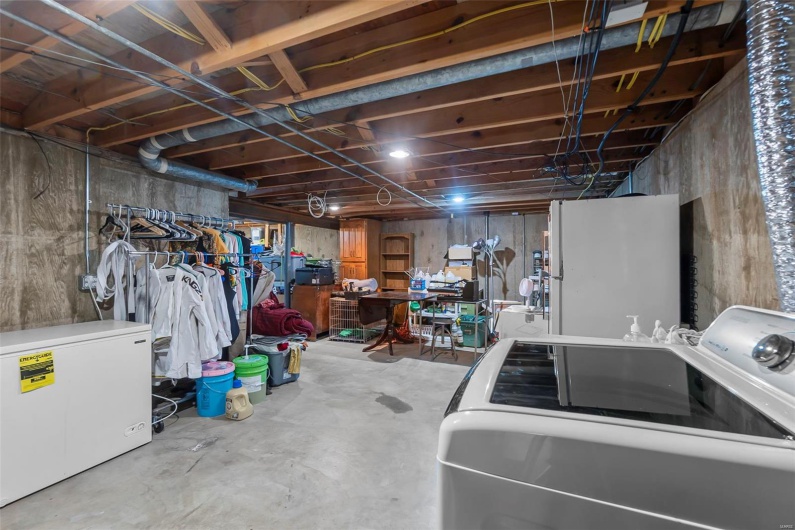 Unfinished basement featuring separate washer and dryer, white fridge, and freestanding refrigerator