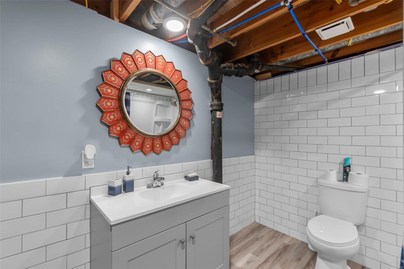 Bathroom featuring toilet, tile walls, visible vents, wood finished floors, and vanity