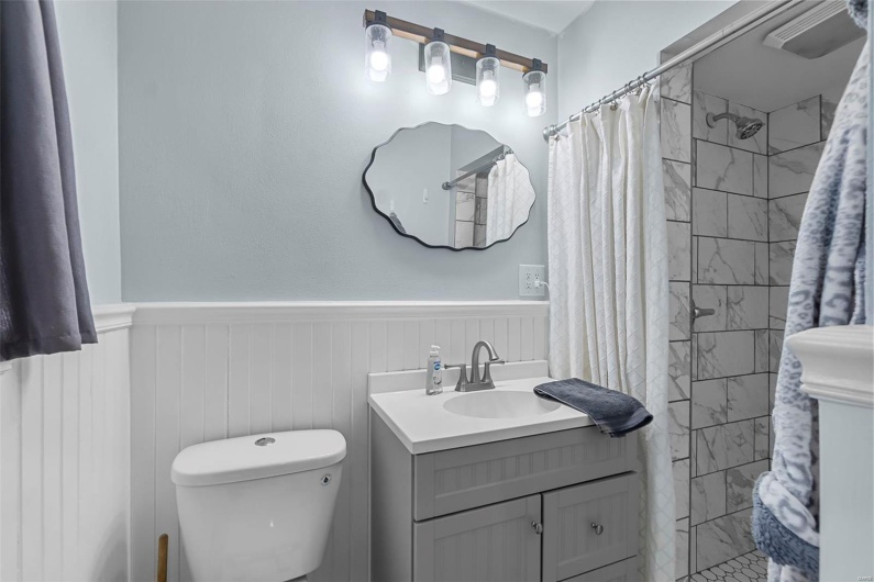 Bathroom featuring vanity, a tile shower, toilet, and a wainscoted wall