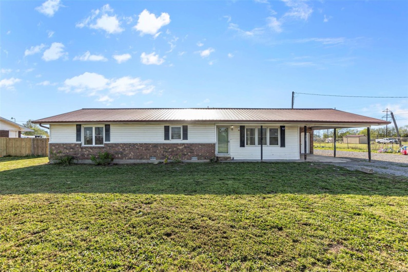 Ranch-style house featuring a front lawn, metal roof, a carport, and fence