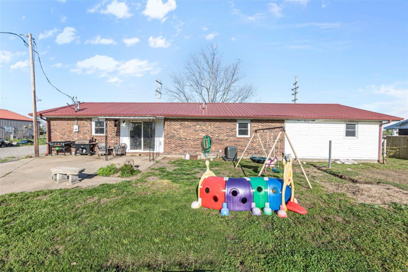 Back of property with central air condition unit, brick siding, fence, and metal roof
