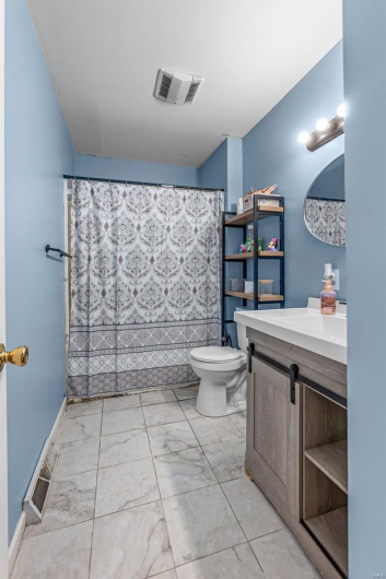 Full bath with marble finish floor, toilet, vanity, and visible vents