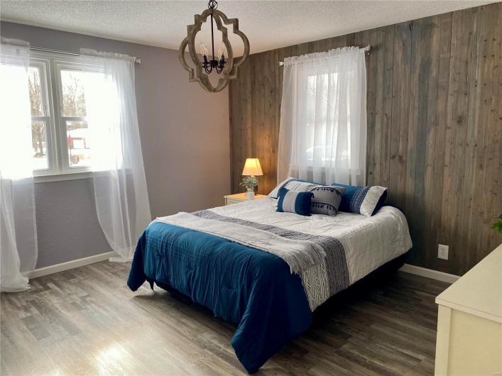 Bedroom with a textured ceiling, an inviting chandelier, hardwood / wood-style floors, and wood walls