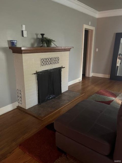 Living room featuring crown molding, a brick fireplace, and dark hardwood / wood-style flooring