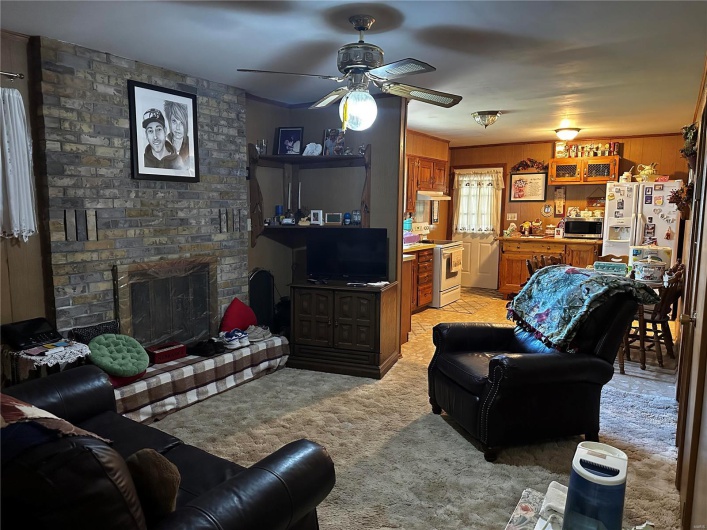 Carpeted living room with a fireplace, wooden walls, and ceiling fan