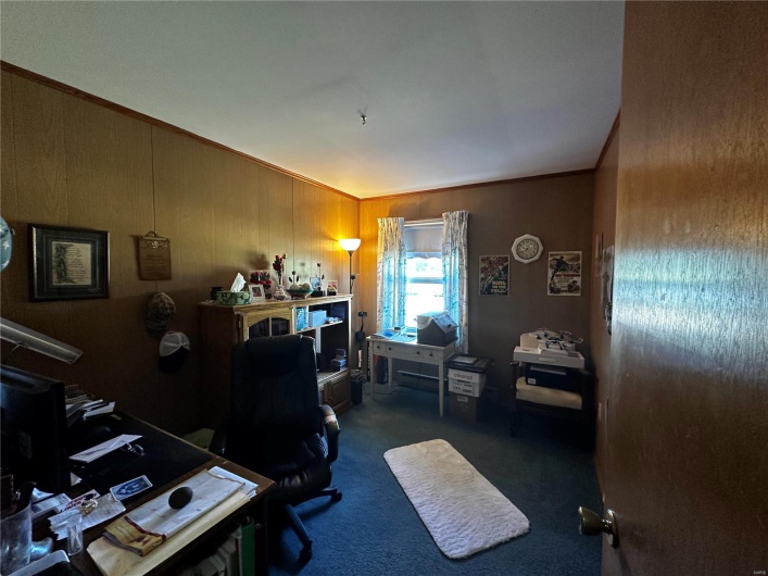 Home office with ornamental molding, wood walls, and dark carpet