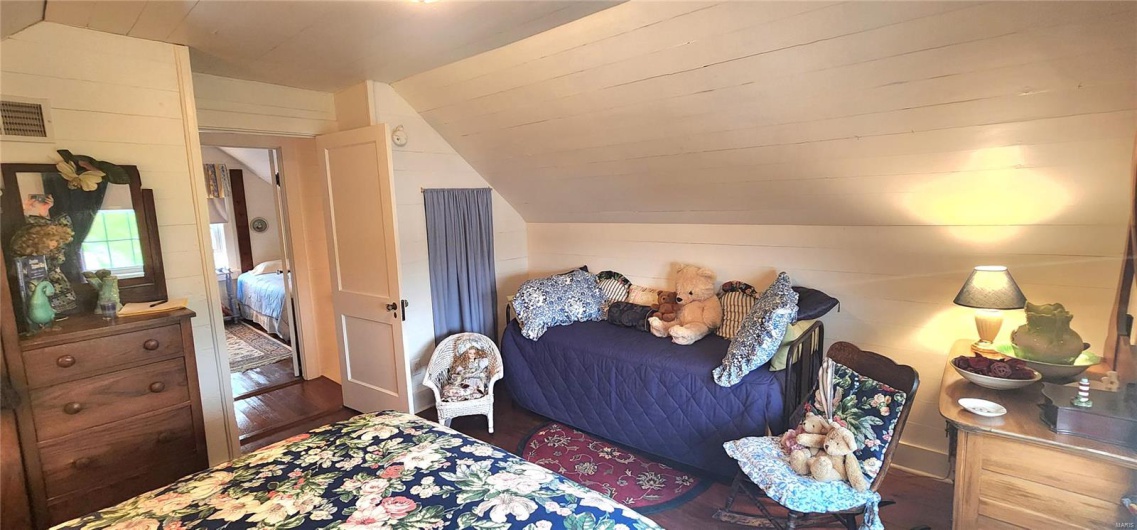 Bedroom featuring lofted ceiling, wood walls, wood finished floors, and visible vents