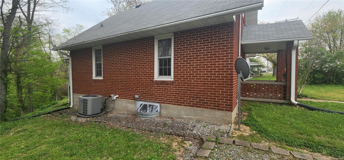 View of home's exterior featuring brick siding, a yard, a shingled roof, and central AC unit