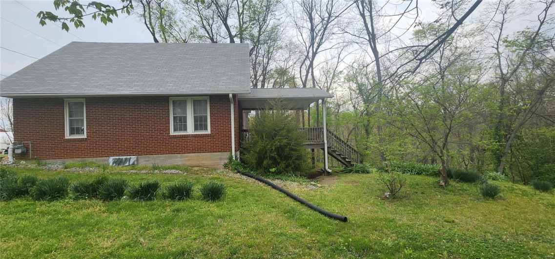 View of side of home with brick siding, a lawn, a porch, and stairway