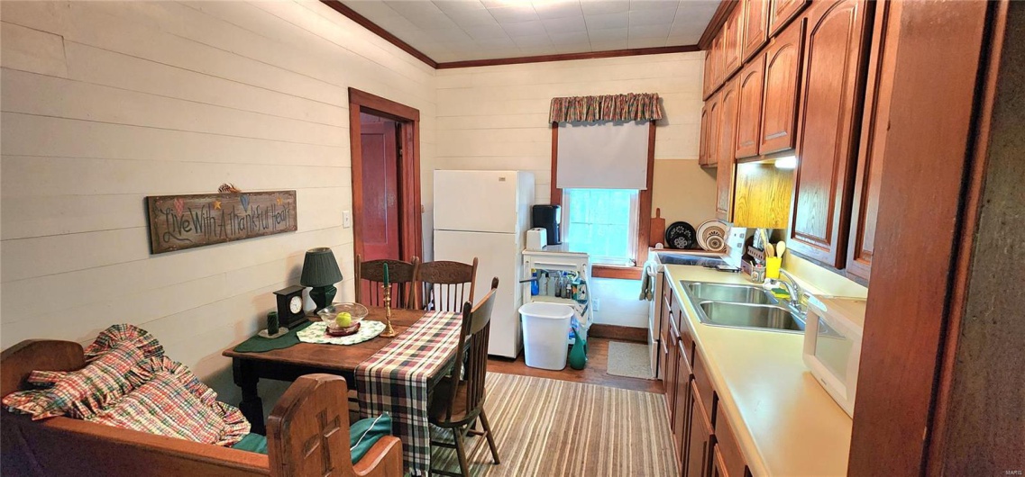 Kitchen featuring white appliances, ornamental molding, wood finished floors, wood walls, and light countertops