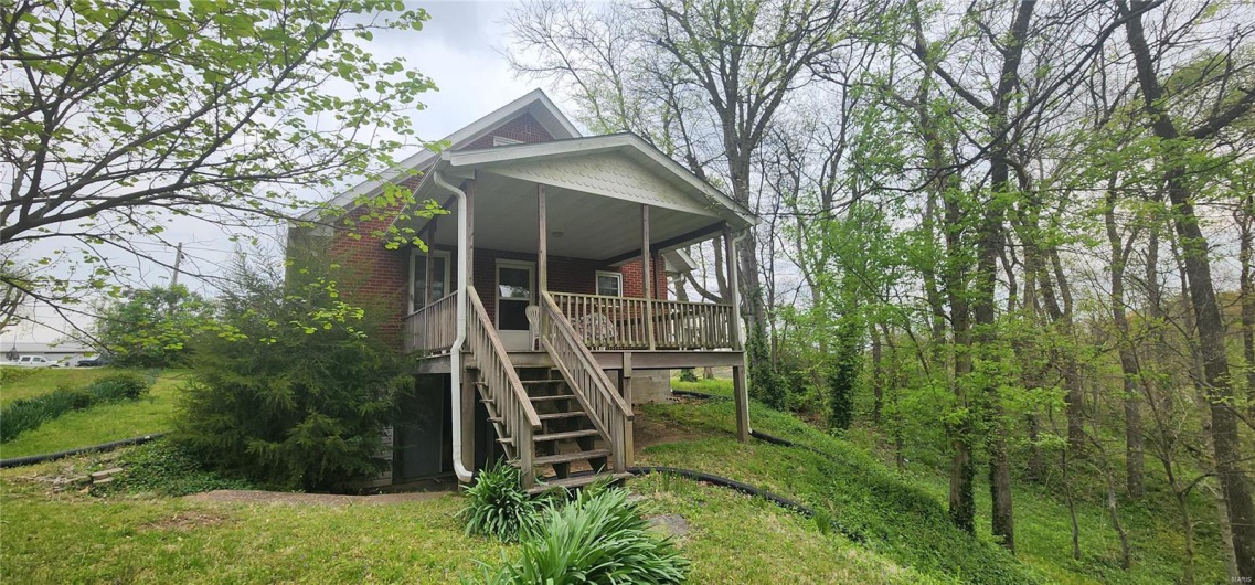 Back of house with a porch, brick siding, and stairs