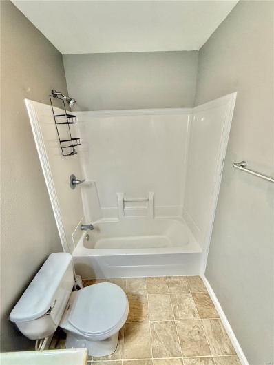 Full bath with stone finish floor, tub / shower combination, and toilet
