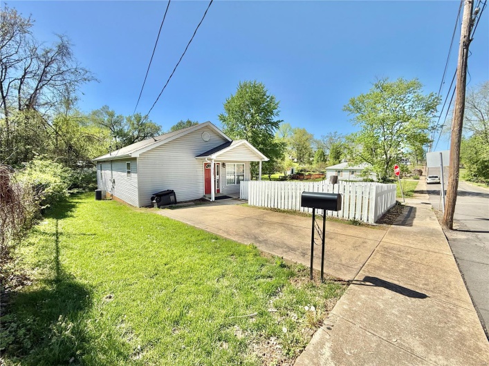 View of side of property with a lawn, fence, and concrete driveway