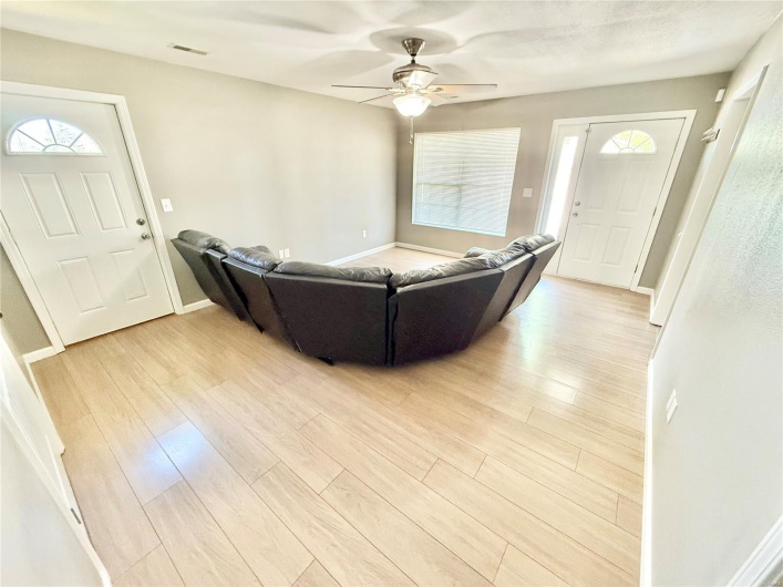 Living room with light wood-style floors, visible vents, a ceiling fan, and baseboards