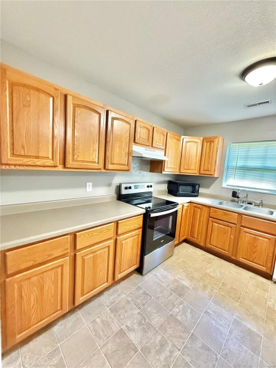 Kitchen featuring a sink, stainless steel range with electric stovetop, light countertops, under cabinet range hood, and visible vents