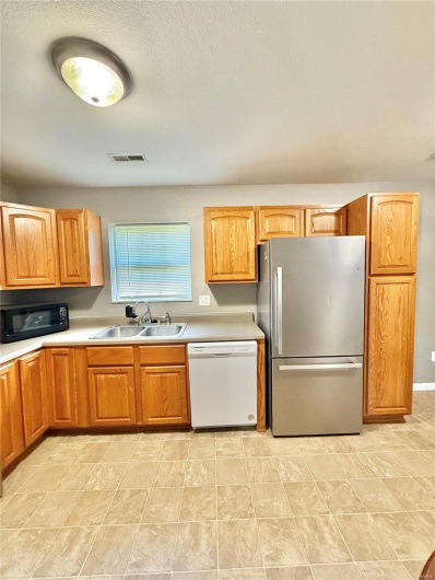 Kitchen with visible vents, a sink, white dishwasher, freestanding refrigerator, and black microwave