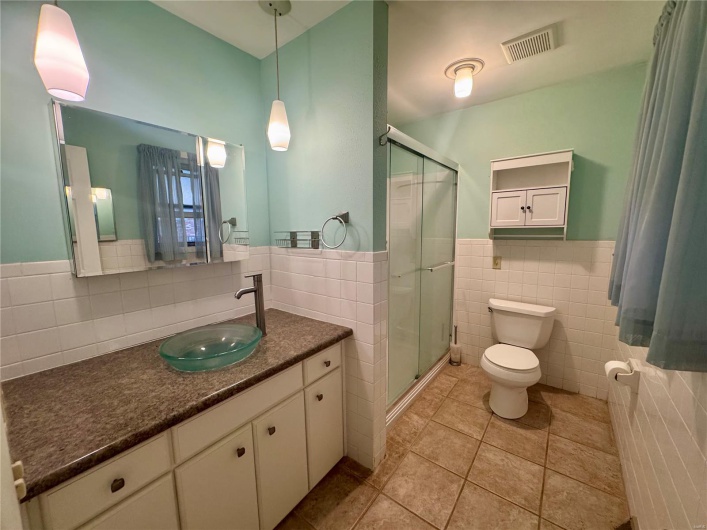 Full bath featuring tile walls, a stall shower, toilet, and visible vents