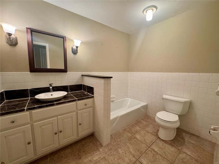 Bathroom featuring tile walls, a wainscoted wall, toilet, and a bath