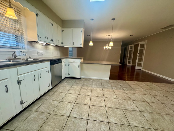 Kitchen featuring stainless steel dishwasher, a peninsula, white cabinetry, a sink, and light tile patterned floors
