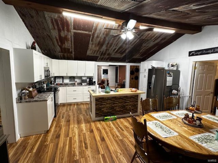 Kitchen with ceiling fan, fridge with ice dispenser, white cabinetry, black range with electric cooktop, and vaulted ceiling with beams