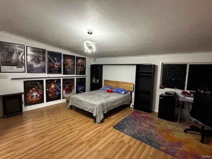 Bedroom featuring vaulted ceiling, hardwood / wood-style flooring, and a textured ceiling